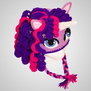 May include: Purple and pink crocheted unicorn hat with a white horn and a braided tail. The hat has a purple and pink mane and a purple and pink face mask.