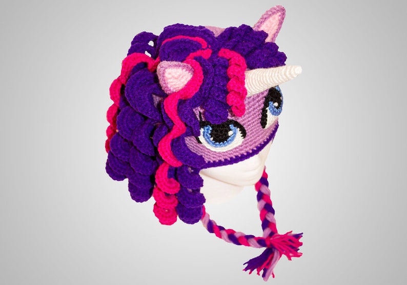 May include: Purple and pink crocheted unicorn hat with a white horn and a braided tail. The hat has a purple and pink mane and a purple and pink face mask.