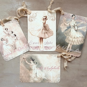 May include: Four vintage-style tags featuring ballet dancers in various poses. Each tag has a cream background with a decorative border and a ribbon for hanging. The tags are labeled "Swan Lake", "La Bayadère", "La Sylphide", and "Pas de Quatre".