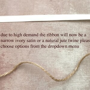 May include: A horizontal white satin ribbon and a length of natural jute twine. The text reads: due to high demand the ribbon will now be a narrow ivory satin or a natural jute twine please choose options from the dropdown menu.
