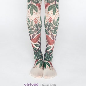 Könnte beinhalten: Weiße Strumpfhosen mit einem Wald-Motiv, das grüne Blätter, rote Beeren und orangefarbene Vögel zeigt. Der Text "virivee - Forest tights" ist unten im Bild gedruckt.