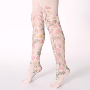 Op de afbeelding: Transparante witte panty met een botanische print van roze en gele wilde bloemen met groene stengels en bladeren. Het bloemmotief loopt van de enkels tot aan de dijen en bedekt de benen met een delicaat, op de natuur ge&iuml;nspireerd ontwerp.