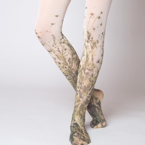 Könnte beinhalten: Undurchsichtige weiße Strumpfhose mit einem botanischen Aufdruck aus grünen und braunen Wildgräsern und Wildblumen, die an den Füßen beginnen und nach oben zu den Oberschenkeln hin verblassen. Das Wort virivee ist unten in kleinen grauen Buchstaben gedruckt.
