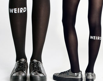 May include: Opaque black tights featuring the word WEIRD printed in white capital letters on the side of the leg. The tights are paired with metallic silver textured sneakers that have black laces and thick black rubber soles.