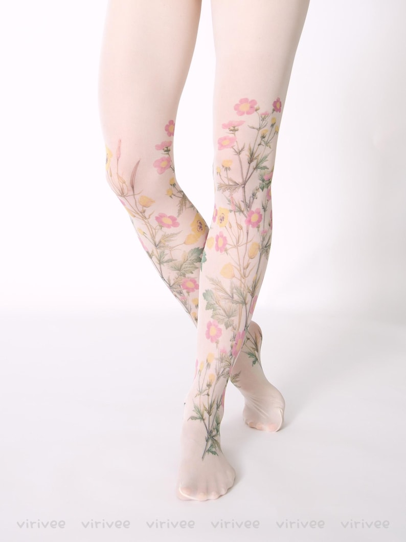 Op de afbeelding: Transparante witte panty met een botanische print van delicate roze en gele wilde bloemen met groene stengels en bladeren. Het bloemmotief loopt van de enkels tot aan de dijen, wat een natuurlijk uiterlijk op de stof cre&euml;ert.
