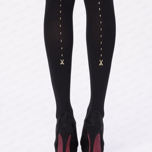 May include: Opaque black tights featuring a vertical gold dashed line running down the back of each leg, ending in a small gold scissor icon near the ankle. The tights are paired with black high-heeled shoes with dark red soles.