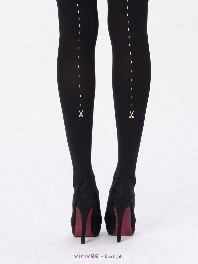 May include: Opaque black tights featuring a vertical gold dashed line running down the back of each leg, ending in a small gold scissor icon near the ankle. The tights are paired with black high-heeled shoes with dark red soles.