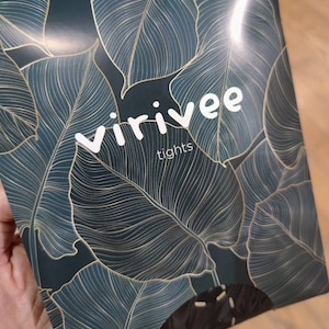 May include: A rectangular product package for Virivee tights featuring a dark teal background with a repeating pattern of large tropical leaves outlined in thin gold lines. The brand name Virivee and the word tights are printed in white text.