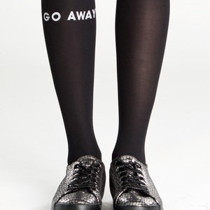 Peut inclure: Collants noirs avec l'inscription "GO AWAY" imprim&eacute;e sur la jambe gauche. Le mannequin porte des baskets noires et argent&eacute;es.