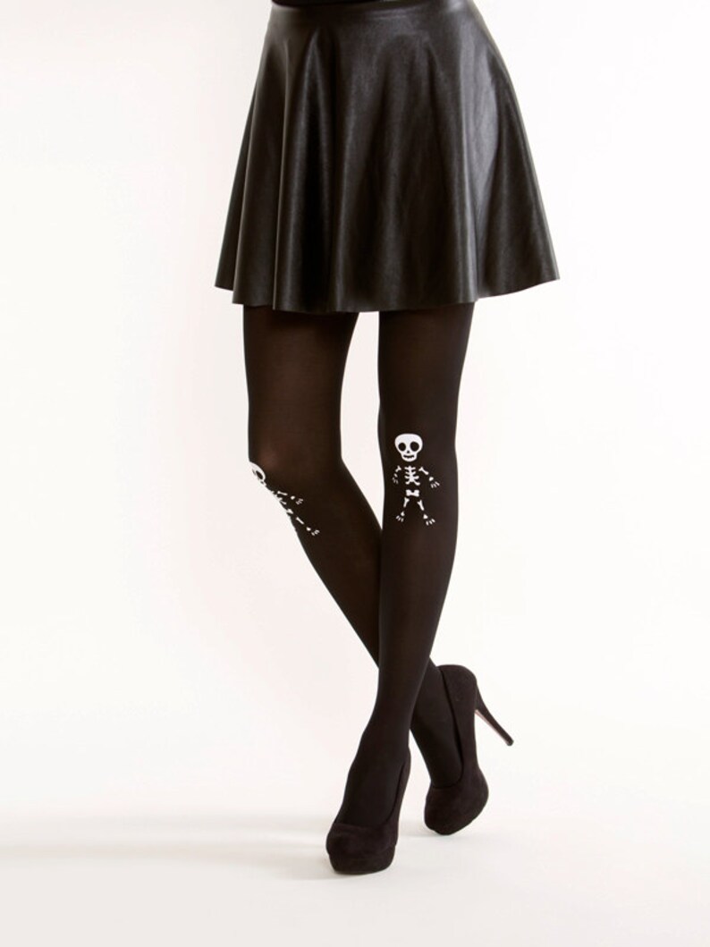 May include: Black opaque tights with a white skeleton design on the legs. The tights are paired with a black leather skirt and black high heels.