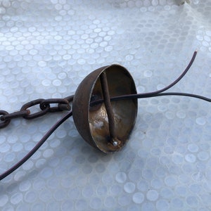 K&ouml;nnte beinhalten: Eine rostige Metallkuppel mit einer Kette, die oben befestigt ist, und zwei schwarzen Dr&auml;hten, die unten herausragen.