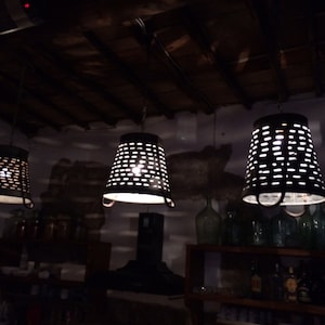 May include: Three metal hanging light fixtures with a perforated design, hanging from a wooden ceiling. The lights are on and casting a warm glow.