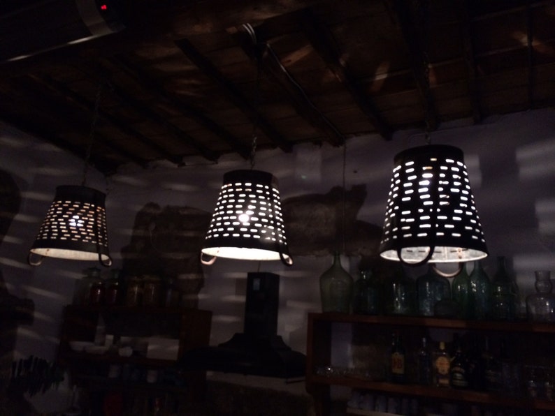 May include: Three metal hanging light fixtures with a perforated design, hanging from a wooden ceiling. The lights are on and casting a warm glow.