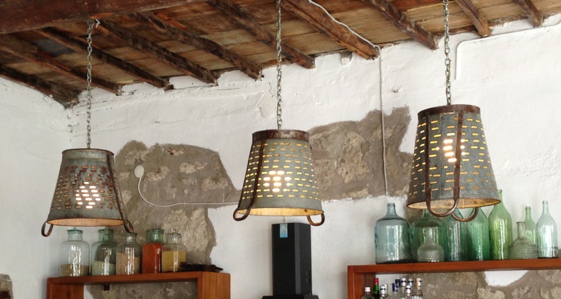 May include: Three rustic metal hanging light fixtures with a whitewashed wood ceiling above. The lights are made from repurposed metal colanders and have a distressed finish.