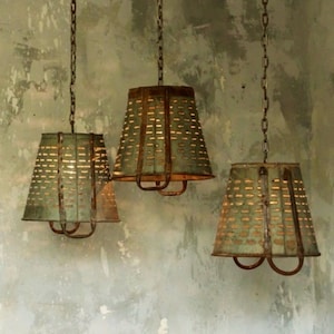 May include: Three rustic metal pendant lights with a distressed green finish and a perforated design. The lights are hanging from chains and have a simple, farmhouse style.
