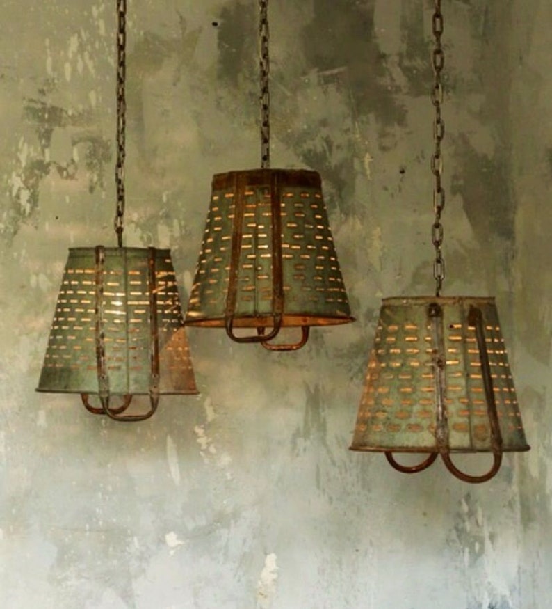 May include: Three rustic metal pendant lights with a distressed green finish and a perforated design. The lights are hanging from chains and have a simple, farmhouse style.