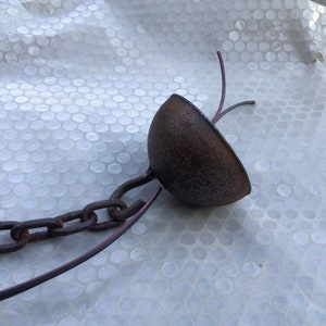 May include: A rusty metal chain with a brown metal dome at the end. The chain is attached to the dome with a hook. Two wires are attached to the dome.