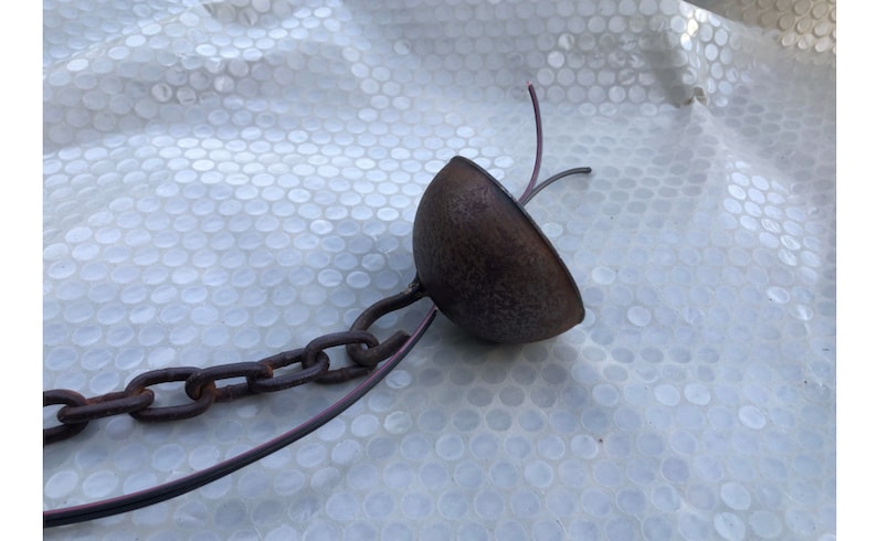 May include: A rusty metal chain with a brown metal dome at the end. The chain is attached to the dome with a hook. Two wires are attached to the dome.