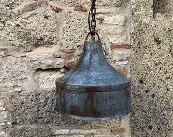 May include: A rustic metal pendant light fixture with a bell-shaped shade, hanging from a chain against a stone wall.