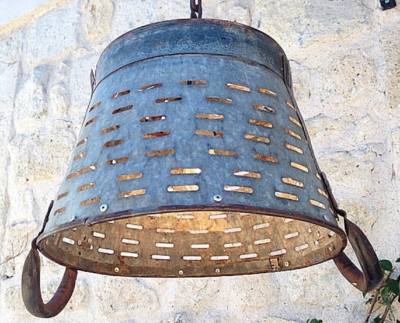 K&ouml;nnte beinhalten: Eine rustikale Metall-Leuchte aus einem wiederverwendeten verzinkten Eimer mit perforiertem Design. Die Leuchte hat zwei Griffe und h&auml;ngt an einer Kette.
