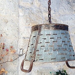 K&ouml;nnte beinhalten: Eine rustikale, h&auml;ngende Leuchte aus Metall, hergestellt aus einem wiederverwendeten verzinkten Eimer mit einer Kette und Haken. Der Eimer hat eine abgenutzte Oberfl&auml;che und ein Muster aus L&ouml;chern.