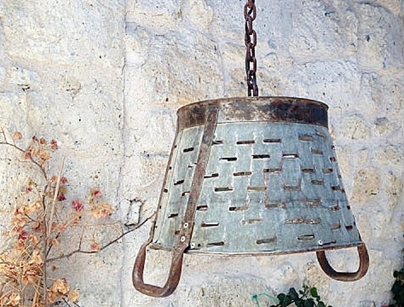 K&ouml;nnte beinhalten: Eine rustikale, h&auml;ngende Leuchte aus Metall, hergestellt aus einem wiederverwendeten verzinkten Eimer mit einer Kette und Haken. Der Eimer hat eine abgenutzte Oberfl&auml;che und ein Muster aus L&ouml;chern.