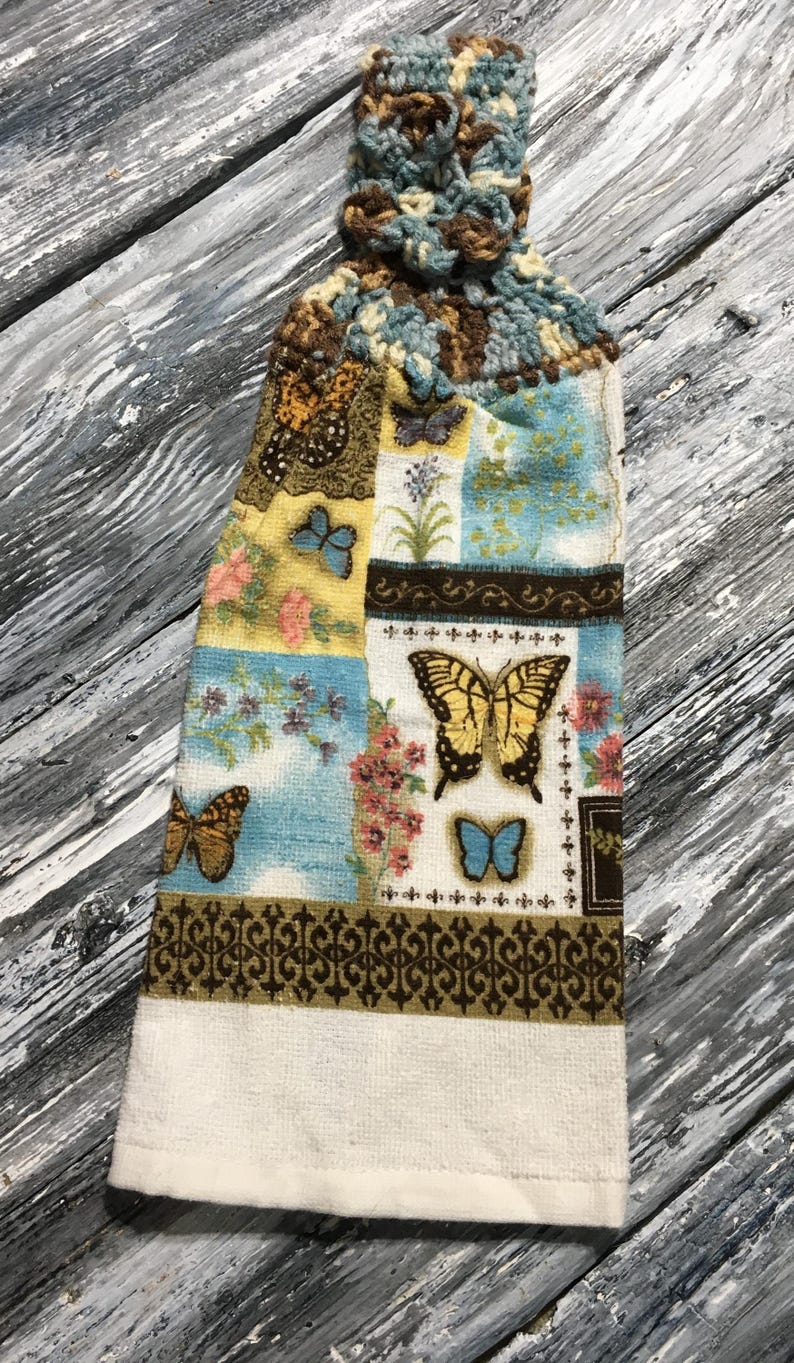 Peut inclure: Un torchon de cuisine d&eacute;coratif avec un dessus crochet&eacute;. Le torchon pr&eacute;sente un motif patchwork avec des papillons, des fleurs et une bordure d&eacute;corative marron. La palette de couleurs comprend le bleu, le jaune et le marron.
