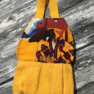 May include: Yellow kitchen towel with a hanging loop. The towel features a colorful print of a Native American woman in traditional clothing.