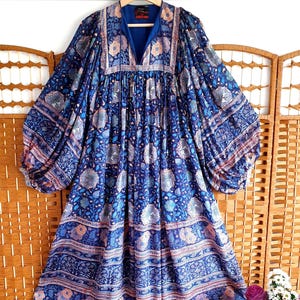 May include: A long-sleeved blue dress with a floral pattern. The dress has a V-neck and a loose, flowing silhouette. The sleeves are long and billowy, and the dress is decorated with a mix of blue, white, and peach floral designs.