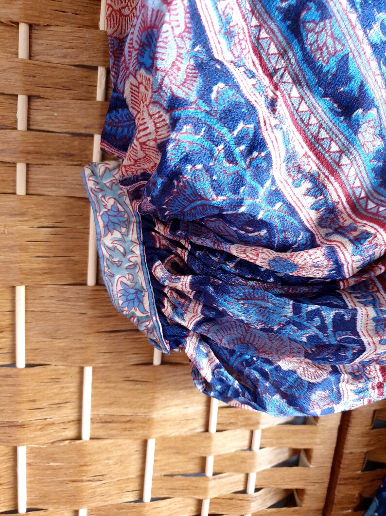 May include: Close-up of patterned fabric in shades of blue, red, and white. The fabric displays a floral and geometric design. The fabric is draped over a woven wooden structure. The pattern is intricate and detailed.