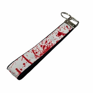 May include: White key chain with a black backing and red blood splatter design.