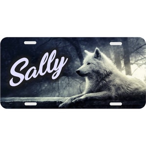 May include: A personalized license plate featuring a white wolf in a dark forest setting. The name "Sally" is written in a white cursive font on the plate.