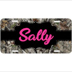 May include: A personalized license plate with a camouflage background. The name "Sally" is written in pink cursive letters on a black background.