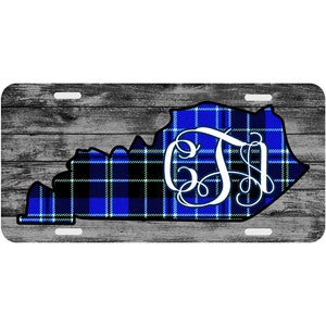 May include: A blue and black plaid Kentucky state outline with a white monogram "CJ" in the center. The outline is on a gray wood background.