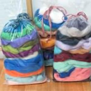 May include: Three clear plastic bags filled with stacked layers of colorful wool roving. Each bag is tied at the top with a string. The wool displays a variety of vibrant hues including blue, green, purple, orange, pink, white, and dark gray.