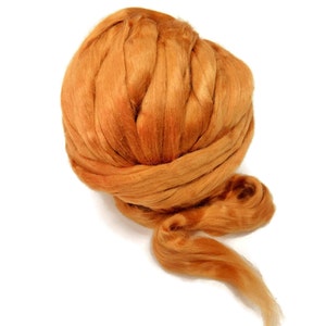 May include: A ball of orange wool fibre, also known as roving, is shown. The wool is loosely packed and has a soft, fluffy texture.
