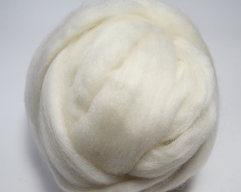 May include: A large, off-white bundle of wool roving, tightly coiled and textured. The fibers appear soft and fluffy, ideal for various crafting projects like felting or spinning. The wool is a natural, undyed color.