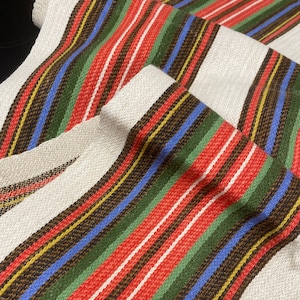 May include: White fabric with red, green, blue, brown, and yellow stripes. The fabric is woven and has a textured surface.