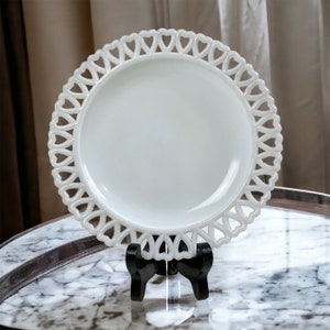 May include: A white milk glass plate with a heart-shaped lace design around the edge. The plate is on a black stand.