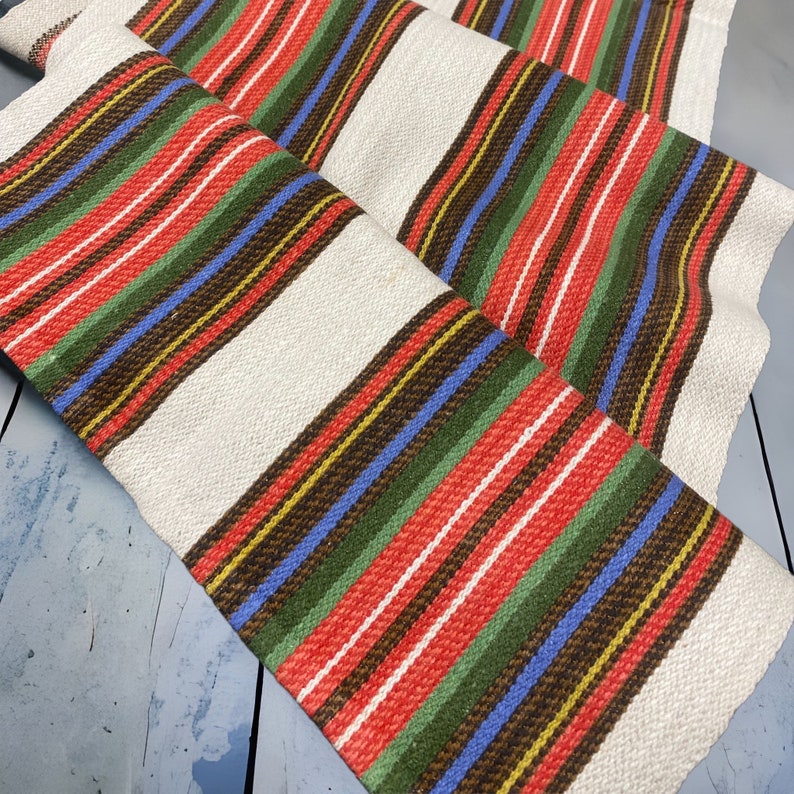 May include: White fabric with red, green, blue, brown, and yellow stripes. The fabric is woven with a pattern of horizontal stripes.