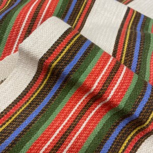 May include: Striped fabric with red, green, blue, yellow, and brown stripes. The fabric has a woven texture.