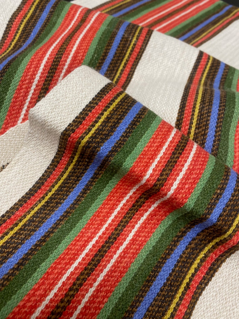May include: Striped fabric with red, green, blue, yellow, and brown stripes. The fabric has a woven texture.