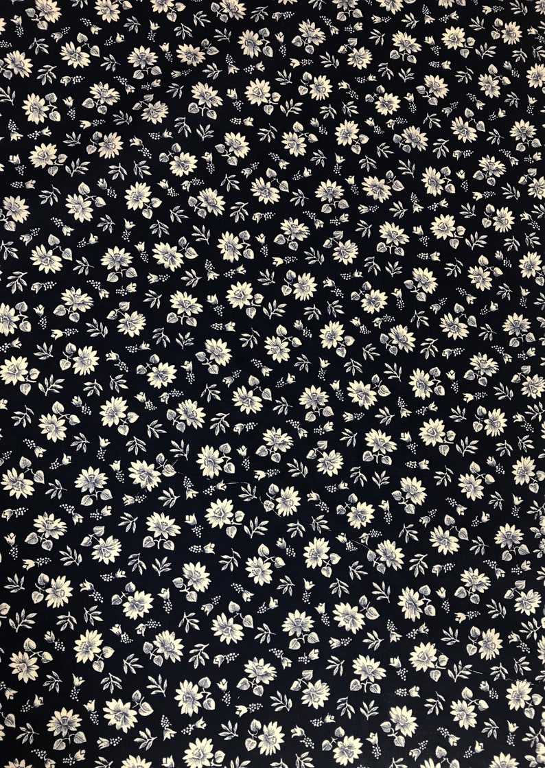 Puede incluir: Una tela negra con un patr&oacute;n floral blanco. El patr&oacute;n presenta peque&ntilde;as flores blancas con un centro amarillo y hojas verdes.