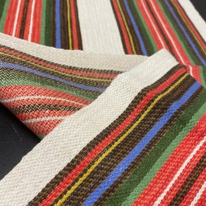May include: A woven fabric with a striped pattern in red, green, blue, yellow, and brown. The fabric has a subtle shimmer.