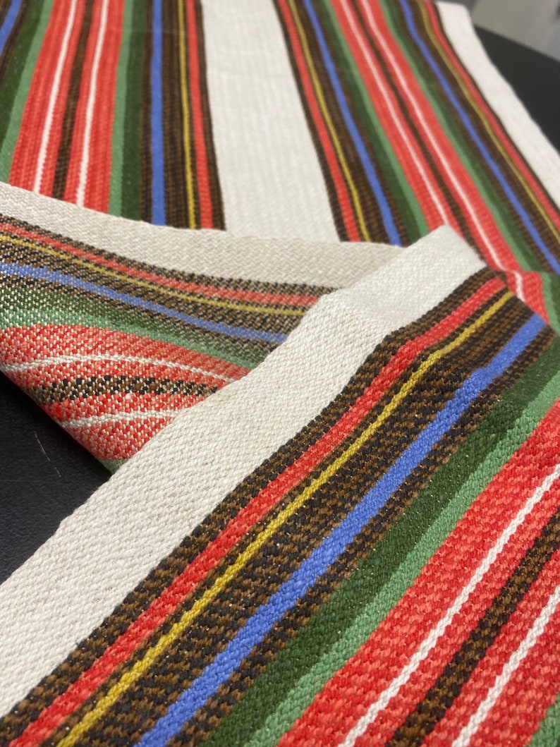 May include: A woven fabric with a striped pattern in red, green, blue, yellow, and brown. The fabric has a subtle shimmer.