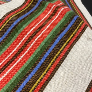 May include: A white fabric with multi-colored stripes in red, green, blue, brown, and yellow. The fabric is woven with a textured pattern.