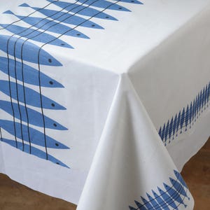 May include: White tablecloth with a repeating pattern of blue fish. The fish are stylized with black lines and dots, creating a nautical theme. The tablecloth is made of a crisp, white fabric.