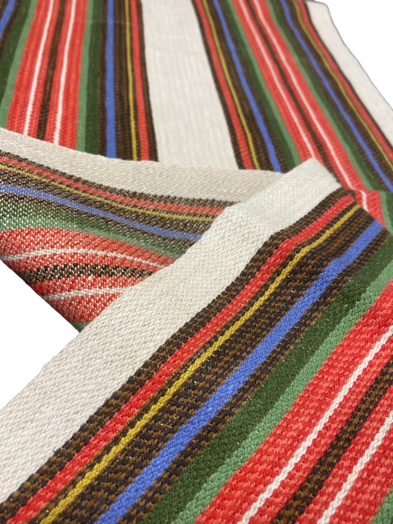 May include: A close-up of a woven fabric with red, green, white, blue, and brown stripes. The fabric has a subtle shimmer and is likely used for a tablecloth or other home decor.