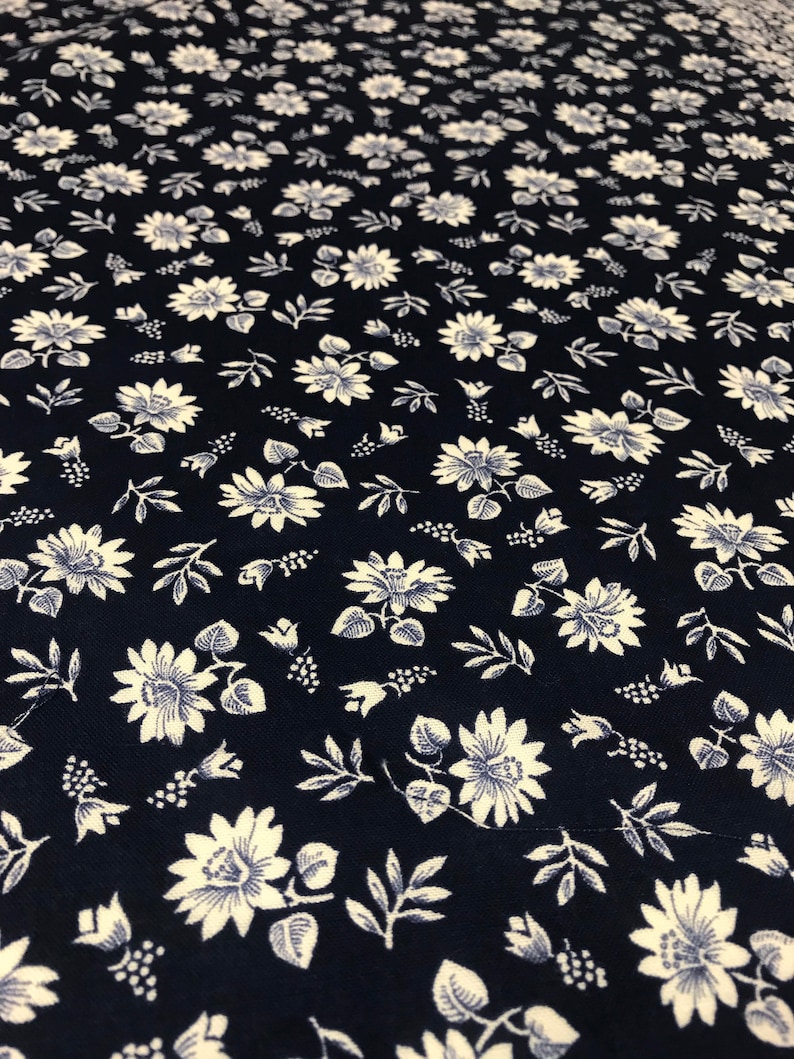 Puede incluir: Una tela azul marino con un patr&oacute;n floral blanco. El patr&oacute;n presenta peque&ntilde;as flores blancas con un centro azul y hojas.