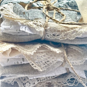 May include: A stack of assorted fabric scraps, including lace and linen, in shades of white, cream, and pale blue. The fabrics are tied together with twine, creating a rustic and vintage aesthetic. Ideal for crafting and textile projects.